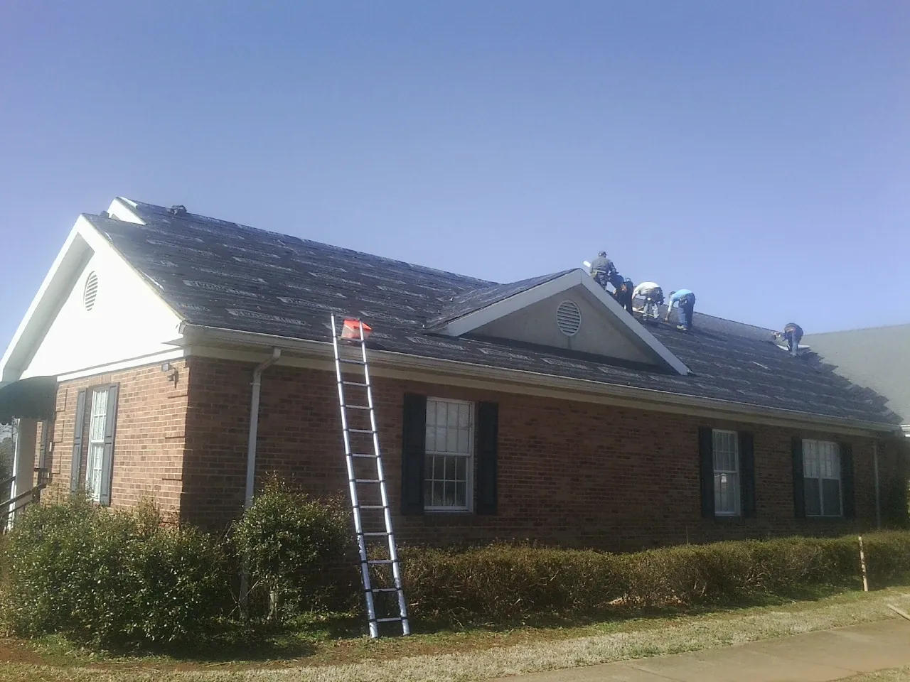 Crew tearing shingles off a brick ranch roof with a ladder set — Emergency Roof Repair work by our crew in Bradley Beach