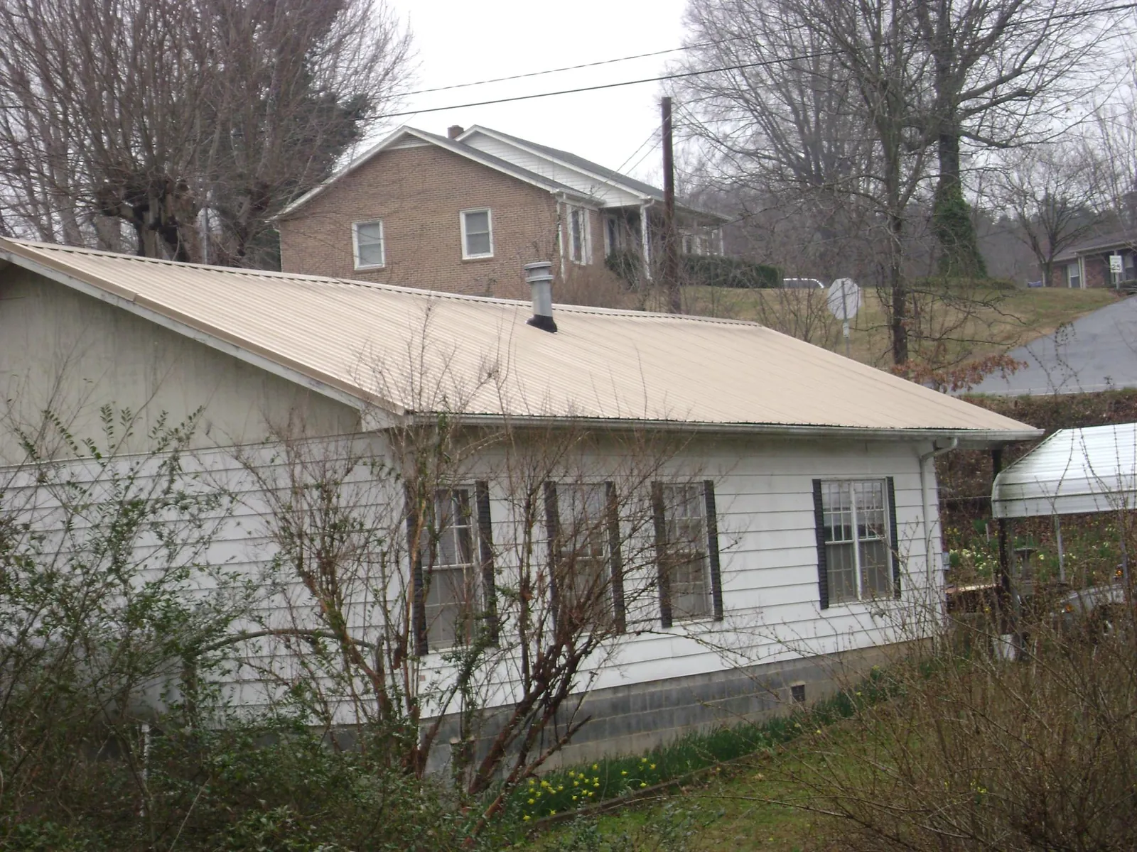 Tan metal roof on a white sided house set into a hillside — Commercial Roofing by Roofing Brothers in Bradley Beach